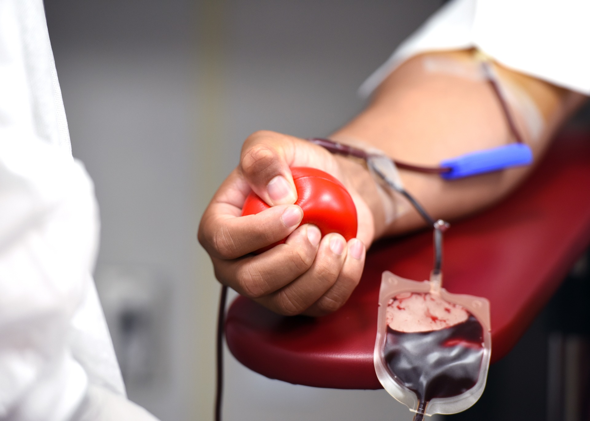 Person squeezing a red ball in their right hand as they receive a blood transfusion