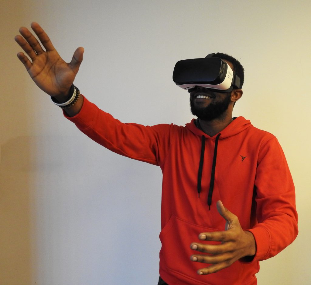 Man in red hoodie wearing a VR headset with right arm reaching up