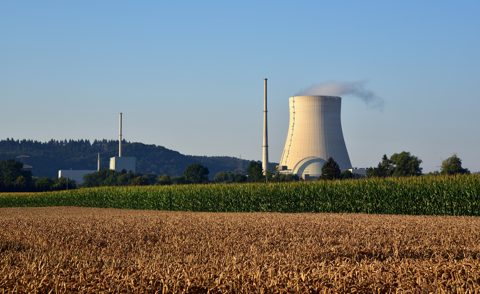 A nuclear power plant with a blue sky and field in foreground.