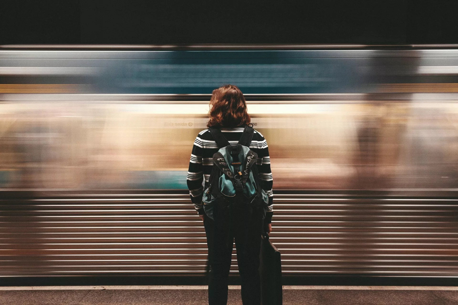 A girl standing in front of a blurry, moving train.