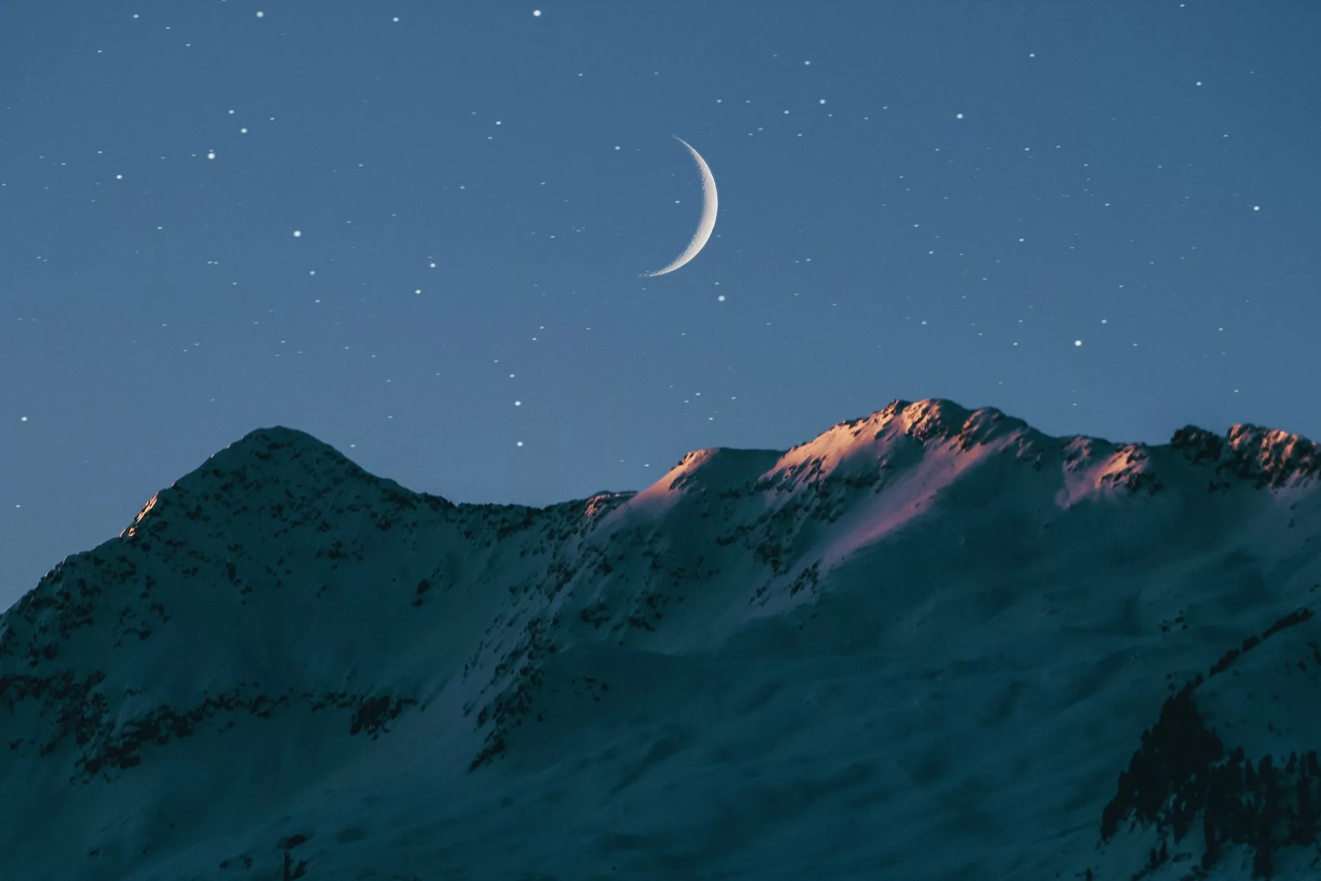 A crescent moon over mountains.